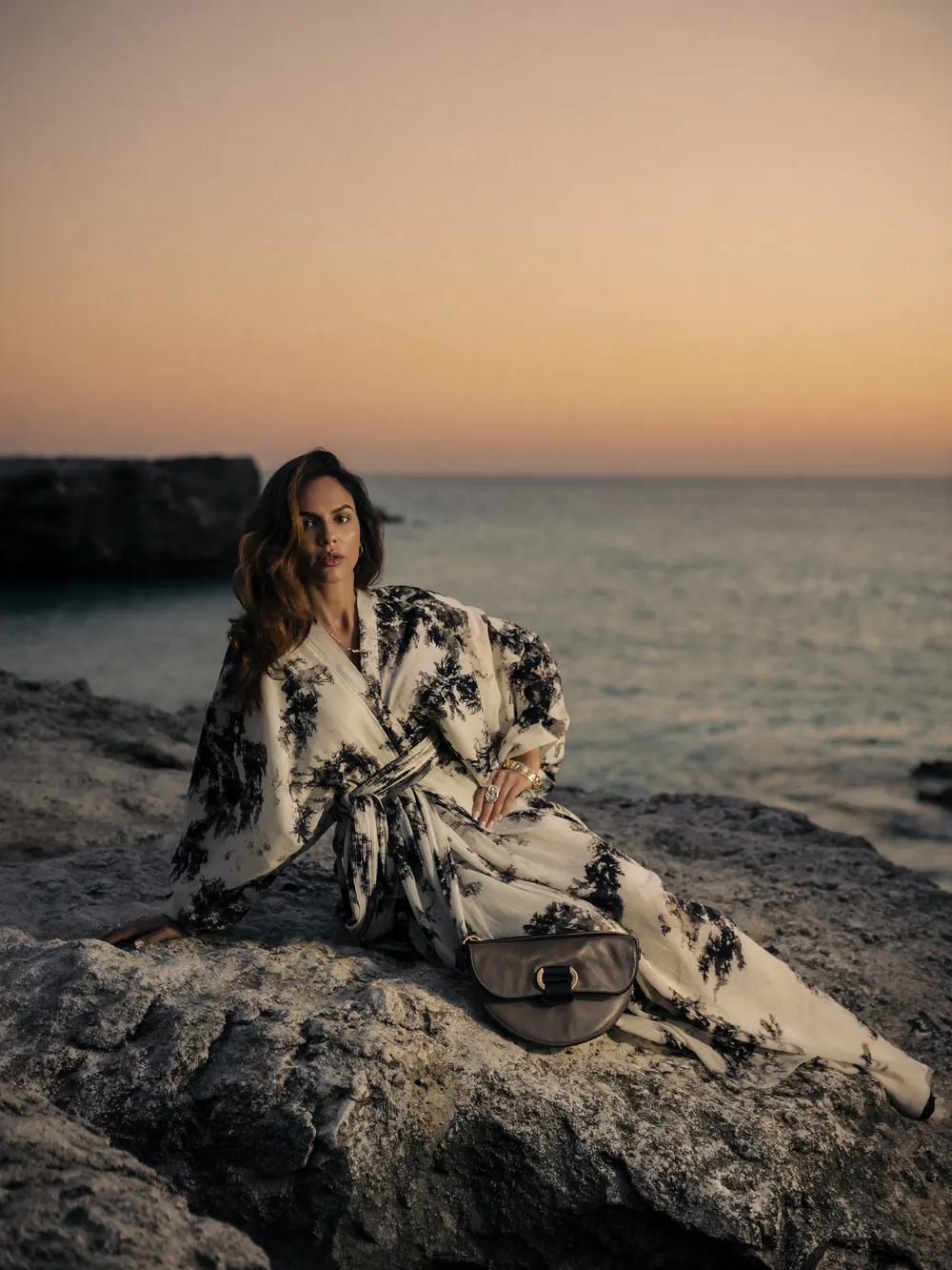 Mujer con kimono estampado sentada en una roca frente al mar